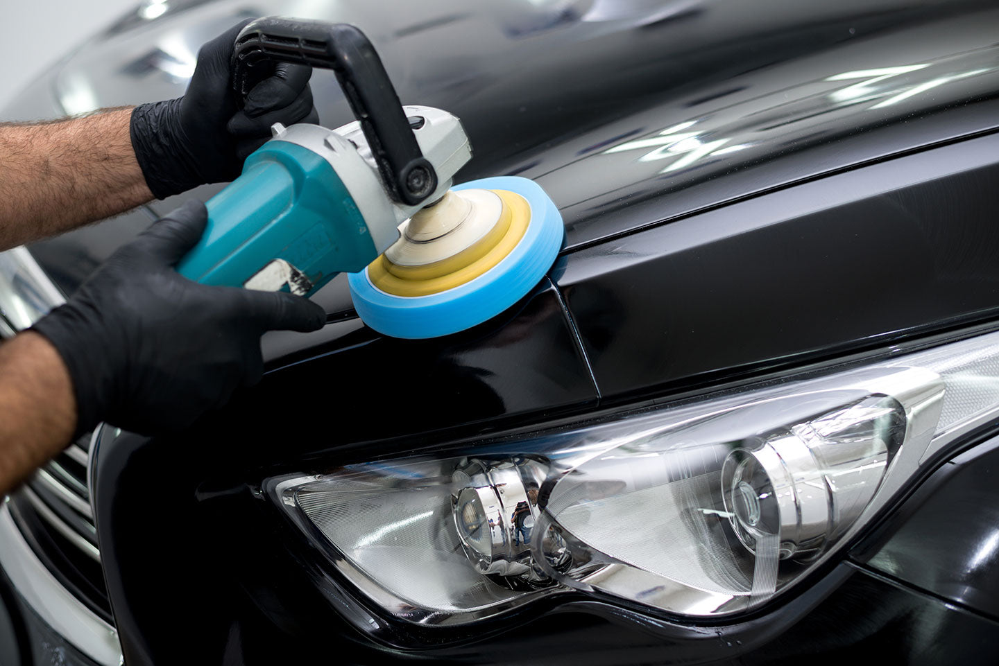 Professional machine polishing a black car bonnet